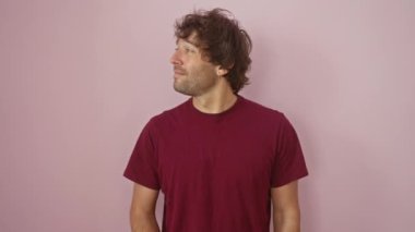 Tişörtlü neşeli, genç İspanyol adam sevinçle işaret ediyor ve yana bakıyor. Arsız pembe bir arka planda mutlu bir gülücük sallayarak.