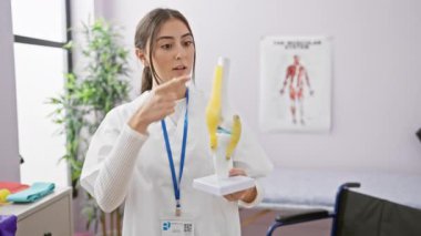 Odaklanmış İspanyol bir kadın, parlak bir rehabilitasyon kliniğinde diz eklemi modelini analiz ediyor..