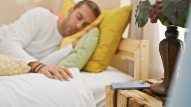 Uyandığında rahat bir yatak odasında telefonuna uzanan yorgun genç bir adam..