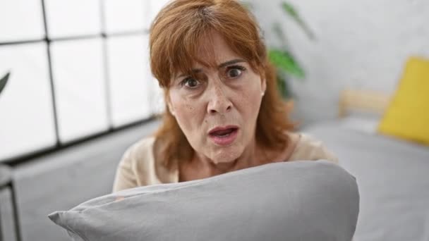 讽刺的中年妇女 满腹狐疑 坐在床上 抱着枕头 茫然不知如何是好 张开嘴 对她在室内的玩世不恭感到惊讶 — 图库视频影像
