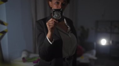 Afrikalı bir Amerikalı kadın dedektif rozetini loş aydınlatılmış bir suç mahallinde gösteriyor. Yetki ve kararlılık yayıyor..