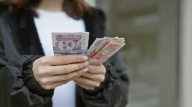 Latin kökenli genç bir kadın, şehir sokaklarında eline ve parasına odaklanarak Kolombiya paralarını sayıyor..