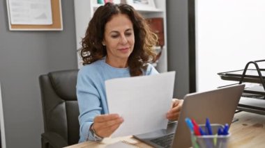 Modern ofis içi bilgisayarında dokümanları inceleyen olgun bir İspanyol kadın..
