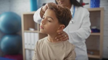 Kadın bir terapist, genç bir çocuğu fizyoterapi kliniğinde muayene ediyor..