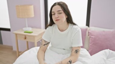 Utanmış, pijamalı genç bir kadın, yatak odasında oturuyor, gözleri negatif jestle kaplıyor, korku ve üzüntüyü ifade ediyor.