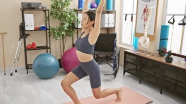 Genç İspanyol bir kadın, iyi donanımlı bir rehabilitasyon kliniğinde yoga pozu veriyor..