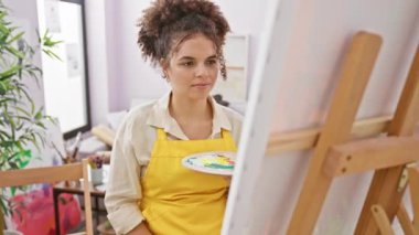 Neşeli, başarılı, kıvırcık saçlı, pozitif ışıldayan, atölyesinde oturan, neşeli, kendine güvenen bir gülümsemesi olan İspanyol kadın sanatçı.