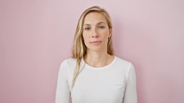 Sarışın bomba şok ve sürpriz yayıyor! Cesur genç bir kadın arsız bir 'ok' hareketi yapar, izole edilmiş pembe bir duvarın arkasından parmaklarının arasından bakar..