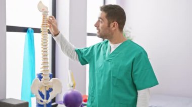 Önlüklü İspanyol adam klinikte omurga modelini analiz ediyor..