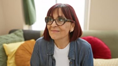 Gülümseyen, orta yaşlı İspanyol bir kadın, düşüncelere dalmış, eve bakıyor, iyimser bir ifade sergiliyor, kendine güveni tam, zeki bir güven ve ilgi karışımı.