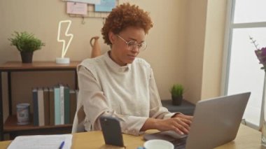 Gülümseyen Afro-Amerikalı kadın zafer işareti yapıyor, rahat oturma odasındaki masasından zafer işareti yapıyor.