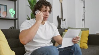 Evde telefonla konuşan genç bir İspanyol, elinde gitar ve arka planda neon levhası olan bir belge tutuyor..