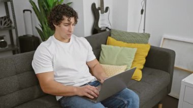 Neşeli, genç İspanyol çocuk evde dizüstü bilgisayarında güvenle internetin tadını çıkarıyor. Oturma odasındaki kanepede otururken sağlıklı, dişlek gülüşünü sergiliyor..