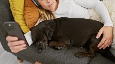 Rahat kadın kulaklıkla müzik dinlerken rahat bir oturma odasında labradoruyla sarılıyor..