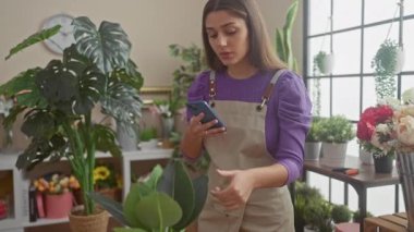 Çiçekçi dükkanında çiçeklerle dolu akıllı telefon kullanan İspanyol kadın..