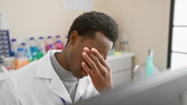 Laboratuvar önlüklü bitkin Afrikalı bir adam laboratuvar ortamında kendini stresli hissediyor, yorgunluk ve sağlık teması sergiliyor.
