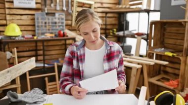 Sinirli sarışın marangoz, öfkeli genç bir kadın, öfke ve stres dolu bir atölyede marangozluk masasında otururken öfkeyle bağırıyor ve bağırıyor..