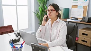 Ofiste çalışan İspanyol bir kadın telefon ve dizüstü bilgisayar kullanıyor.