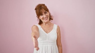 Orta yaşlı, kendine güvenen, pembe elbiseli, pembe arka planda izole edilmiş başarılı bir tokalaşma sunan iş kadınına hoş geldin diyoruz.