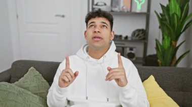 Keyifli genç Arap adam, evde giyinmiş, şaşkınlık ve şaşkınlık içinde sevinçle işaret ediyor.!