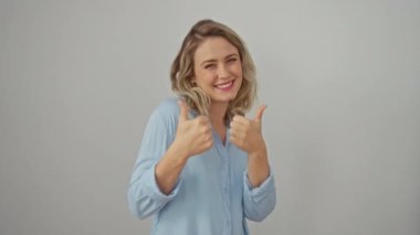 Çekici bir gülümsemesi olan neşeli genç sarışın kadın, beyazlar içinde duruyor, başarı belirtileri gösteriyor, olumlu jestler yapıyor, kendinden geçmiş ve mutlu.