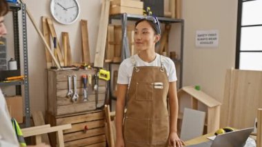 İki marangoz, bir erkek ve bir kadın, iyi donanımlı bir marangoz atölyesinde iş birliği yapıyorlar, fikirleri paylaşıyorlar ve el sıkışıyorlar..