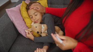 Şefkatli bir kadın, rahat bir oturma odasındaki kanepede uyuyan bir çocuğu nazikçe rahatlatır. Anne sevgisini ve aile sıcaklığını sembolize eder..