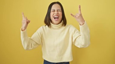 Çılgınca! Güzel, genç İspanyol bir kadın, rock müzik yıldızı konsepti, ağır metal sembolü, sarı izole edilmiş arka plana karşı soğuk bir süveterin içinde duran.