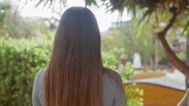 Yeşil bir parkta, açık havada kahverengi saçlı genç bir kadının arka görüntüsü.