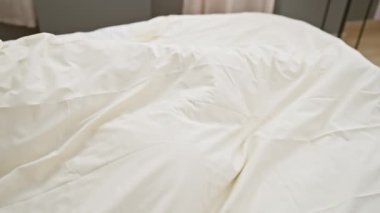 Genç bir adam, beyaz, rahat bir yatak odasında huzur içinde uyuyor. Etrafı yumuşak yatak örtüsü ve sakin bir ortam ile çevrili..