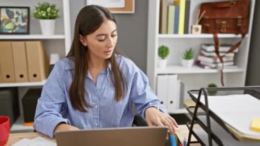 Genç bir İspanyol kadın, iç mekan ofisinden neşeli bir video görüşmesi yapıyor. Çekici ve neşeli bir iş ortamını canlandırıyor..