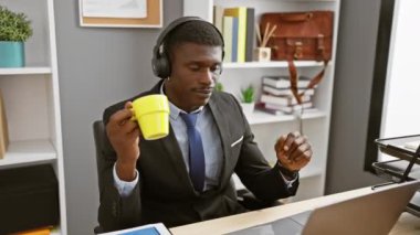 Kulaklıklı yakışıklı Afrikalı adam modern bir ofiste kahveden hoşlanıyor..