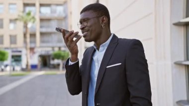 Takım elbiseli Afro-Amerikan işadamı şehir caddesinde akıllı telefon kullanıyor.