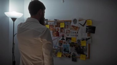 Ofiste suç tahtasını analiz eden sakallı bir adamın arka görüntüsü..