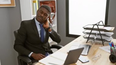 Ofis masasında oturan takım elbiseli yakışıklı Afrikalı bir adam, boyun rahatsızlığı çekiyor.