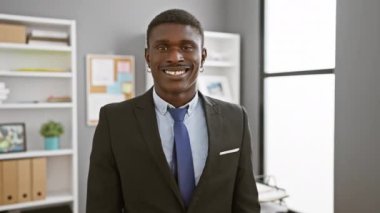 İş kıyafetleri giymiş, modern ofis ortamında güvenle gülümseyen Afrikalı bir Amerikalı..