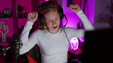 Neşeli genç bir kadın canlı, neon ışıklı bir odada kulaklık takarak oyun oynarken kutlama yapıyor..