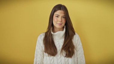 Süveter giymiş genç, güzel bir İspanyol kadının portresi, izole edilmiş sarı bir arka planda sıcak, misafirperver bir gülümsemeyle yardım eli uzatıyor..