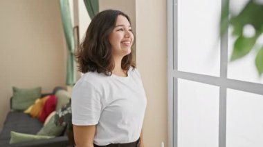 Kendine güveni tam genç İspanyol bir kadın, evinde rahat, rahat bir poz veriyor, doğal bir gülümsemeyle ışıldıyor..