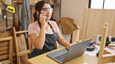 Atölyede telefon ve dizüstü bilgisayar kullanan İspanyol kadın marangoz.
