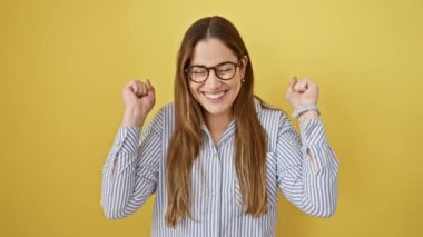 Mavi gözlü ve gözlüklü kendinden geçmiş genç bir kadın, muazzam başarısını kutluyor, sarı arka planda tek başına duruyor, neşeli bir şekilde evet diye bağırıyor..