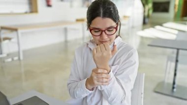Genç İspanyol bir kadın, modern işyerinde dizüstü bilgisayarının başında otururken bilek ağrısı çekiyor..