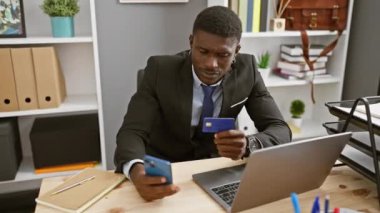 Takım elbiseli profesyonel bir Afrikalı. Akıllı telefonu ve kredi kartı olan. Ofis masasında dizüstü bilgisayarı ve defteri olan..