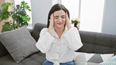 Sıkıntılı bir İspanyol kadın evdeki bir kanepede oturur. Stres, rahatsızlık ve ev içini gösterir..