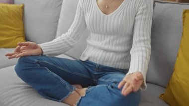 Kafkasyalı genç bir kadın rahat oturma odasındaki kanepede meditasyon yapıyor..