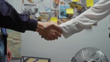 Arka planda soruşturma kuruluyla bulanık bir ofiste el sıkışan erkek ve kadın.