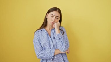 Güzel, genç, İspanyol bir kadın, yorgun ve sıkılmış, depresyon sorunları hakkında düşüncelere dalmış, kolları çapraz sarı arka planda gömlek giyiyor..