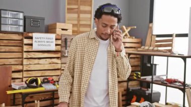 Marangozluk atölyesinde sıradan kıyafetler ve güvenlik gözlüğü takan genç bir adam arıyor.