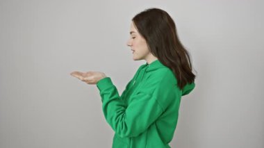 Sweatshirt 'lü heyecanlı genç bir kadın. Avuç içi açık bir şekilde reklam alanına bakıyor. İzole edilmiş beyaz arkaplana karşı neşeyle bir ürün sunmak.