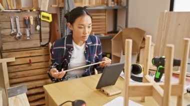 Çinli kadın, dijital tablet kullanarak, iyi donanımlı bir marangozluk atölyesinde ahşabı inceliyor.